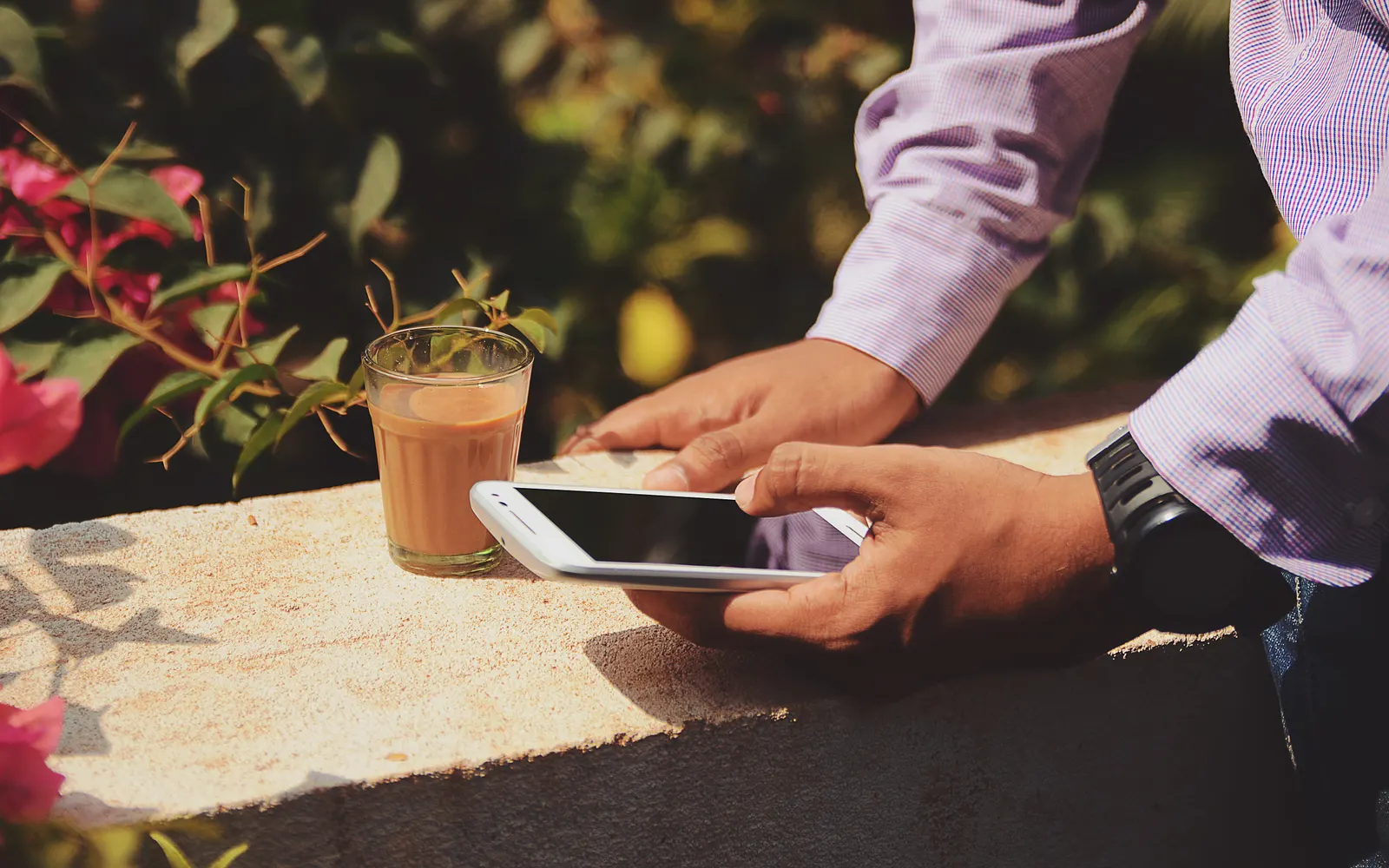 Hands holding a smartphone beside a glass of tea outdoors