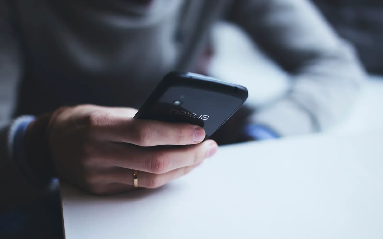 A person holding a black Android phone in one hand at a white desk
