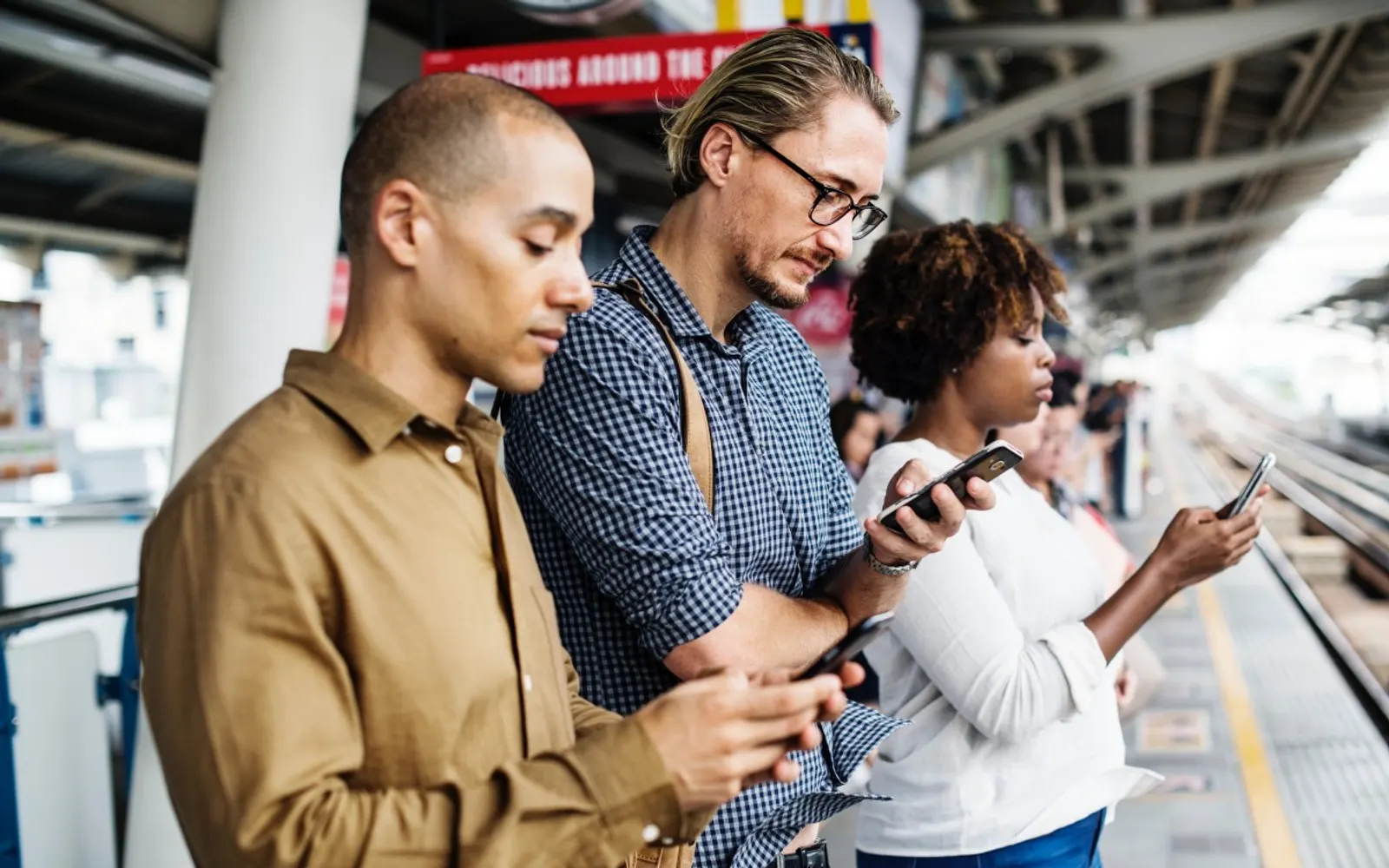 Three commuters of different backgrounds standing together, each looking at their phone