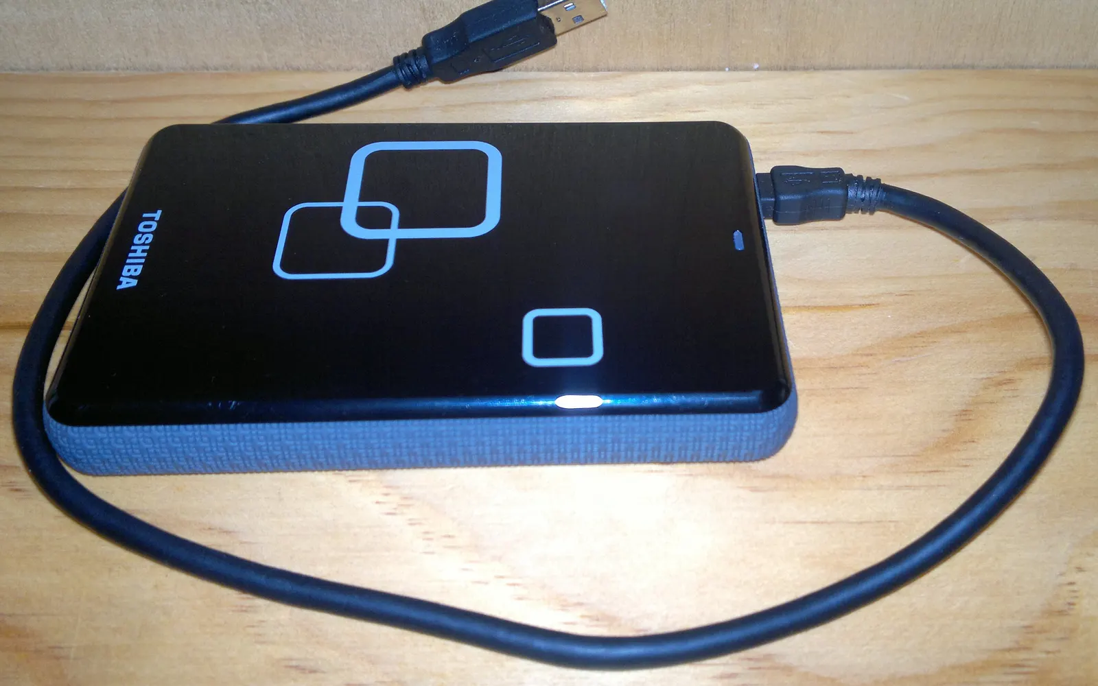 A portable hard drive with its USB cable on a wooden desk