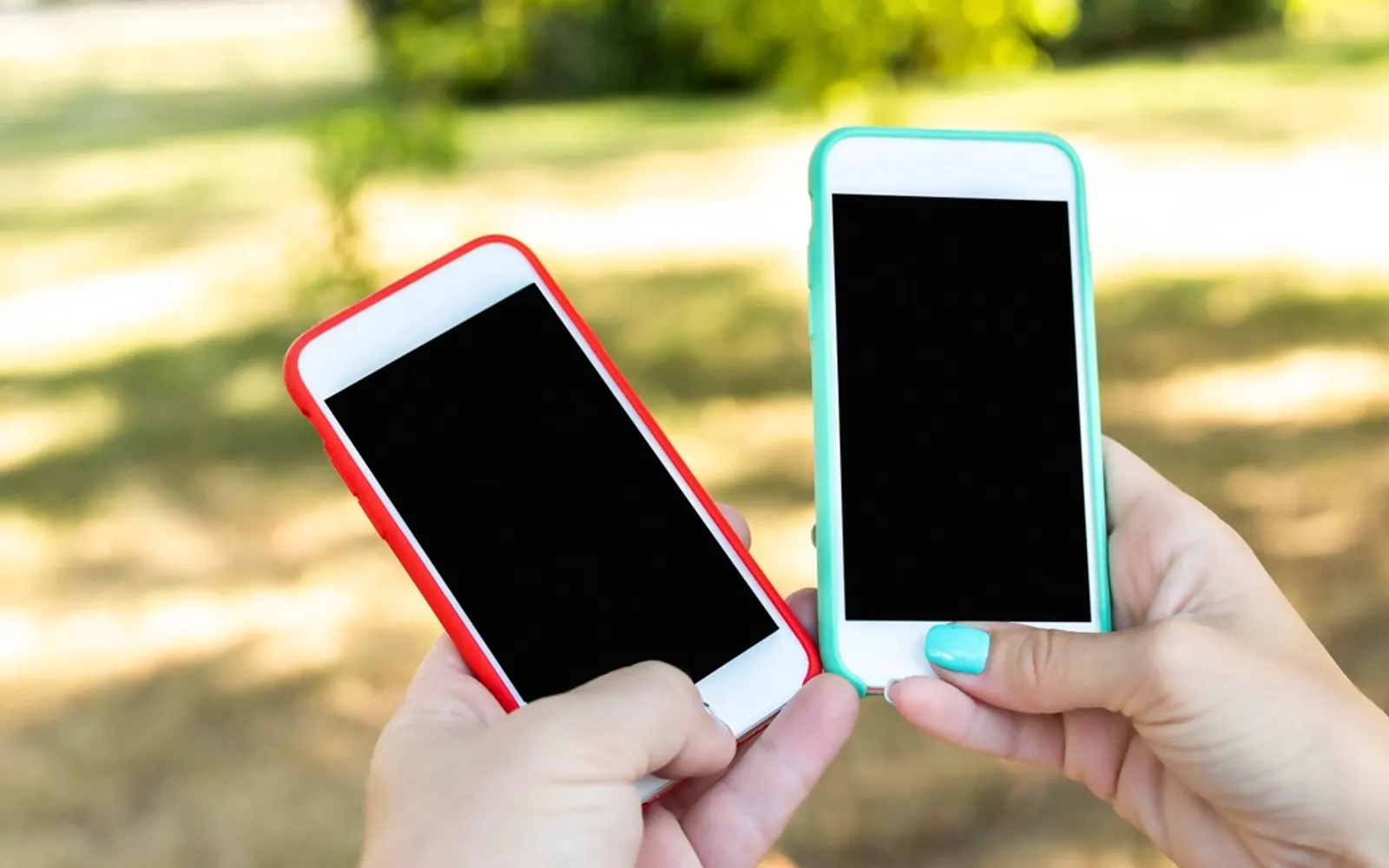 Two hands holding smartphones with blank screens side by side outdoors