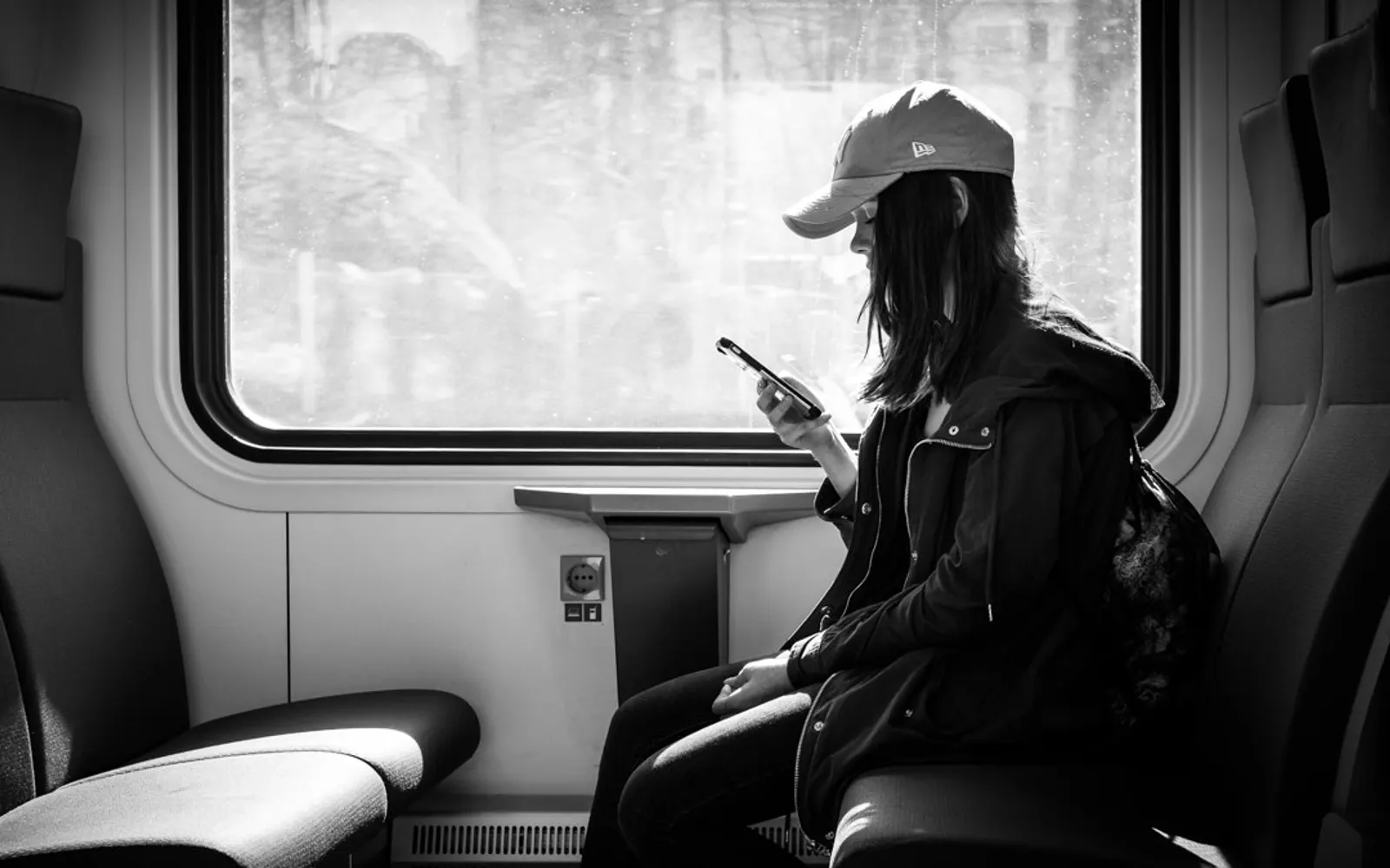 A woman in a cap looking at her phone while riding a train, in black and white
