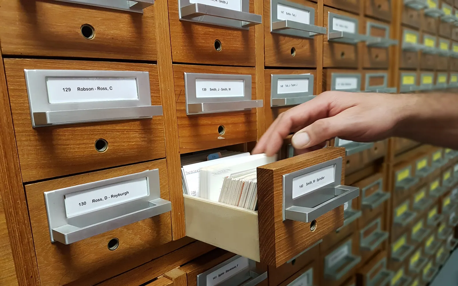 A hand pulling a drawer out of a wooden card catalogue