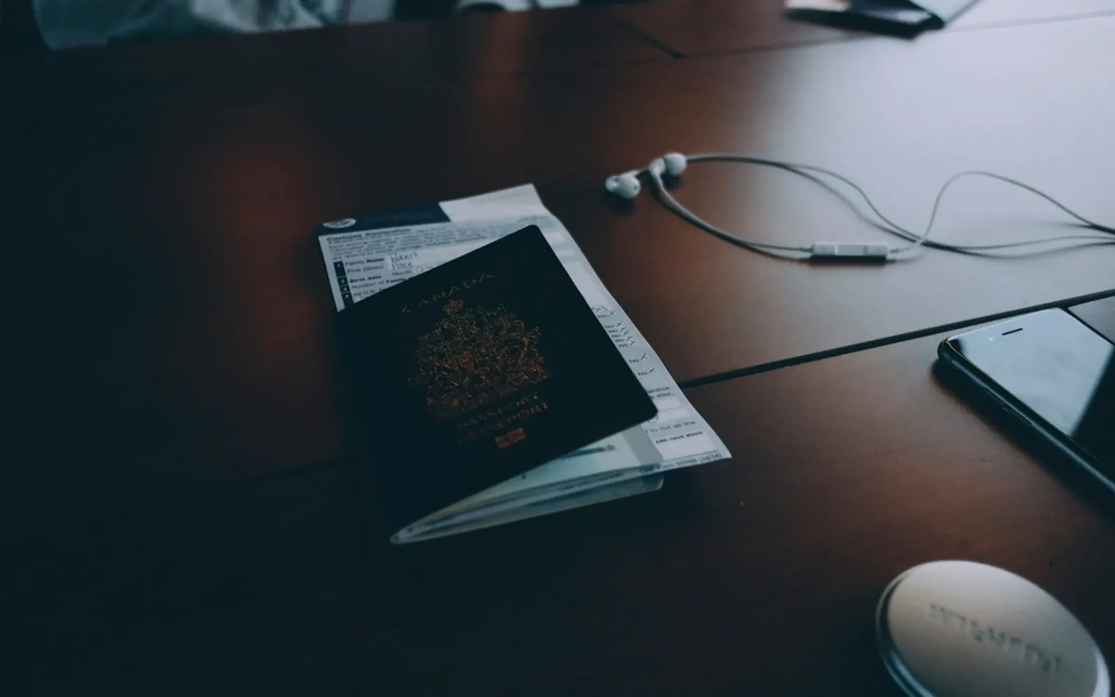 A passport, papers and earphones lying on a dark desk