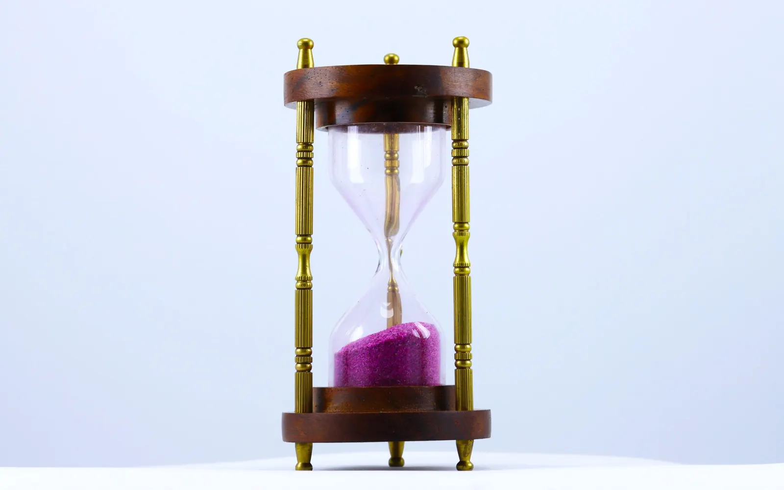 An hourglass with pink sand on a white background