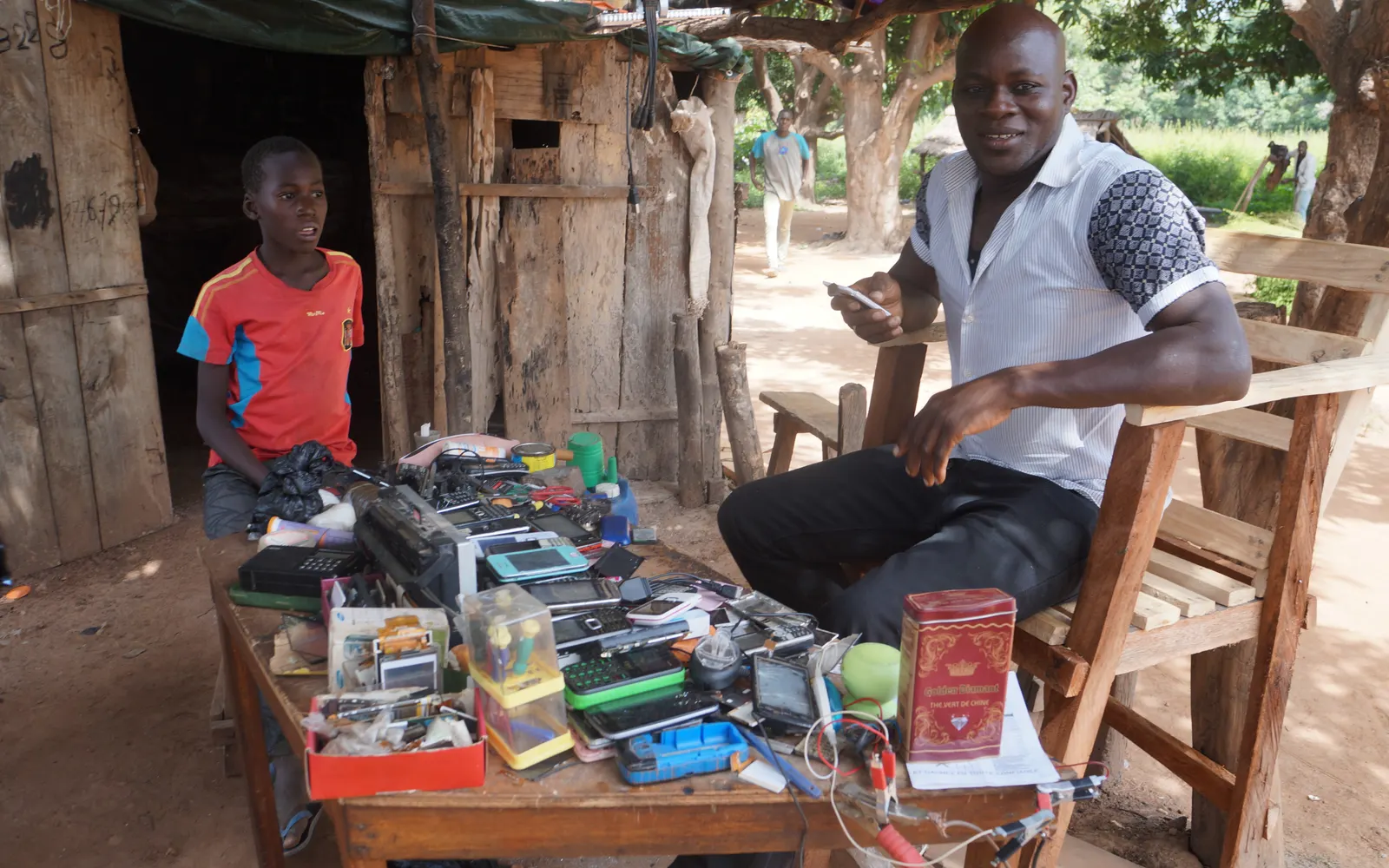 A trader and a boy at an outdoor stall of second-hand phones and parts