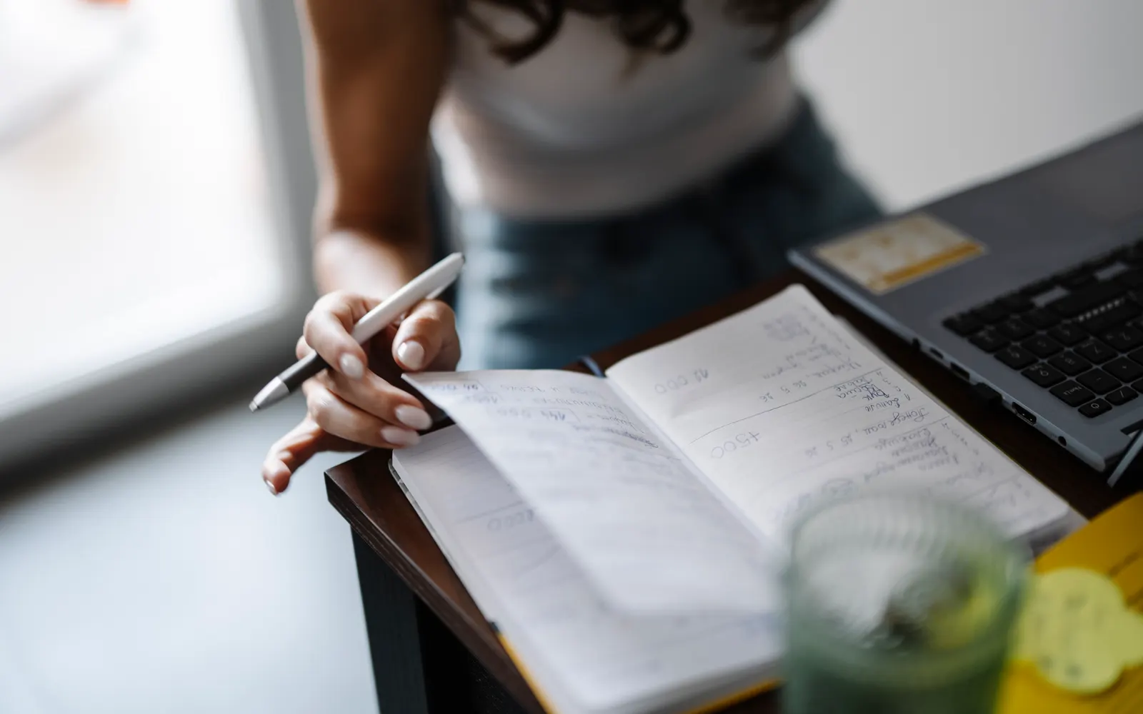 A woman writing notes in a journal beside a tablet