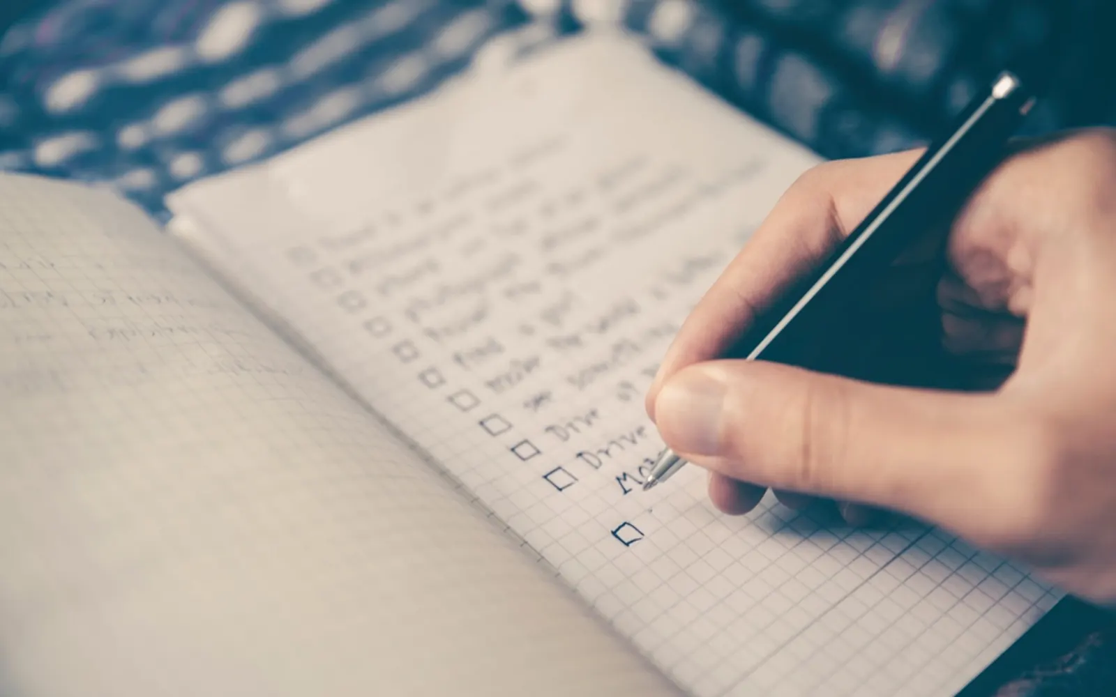 A hand writing a checklist in a squared notebook