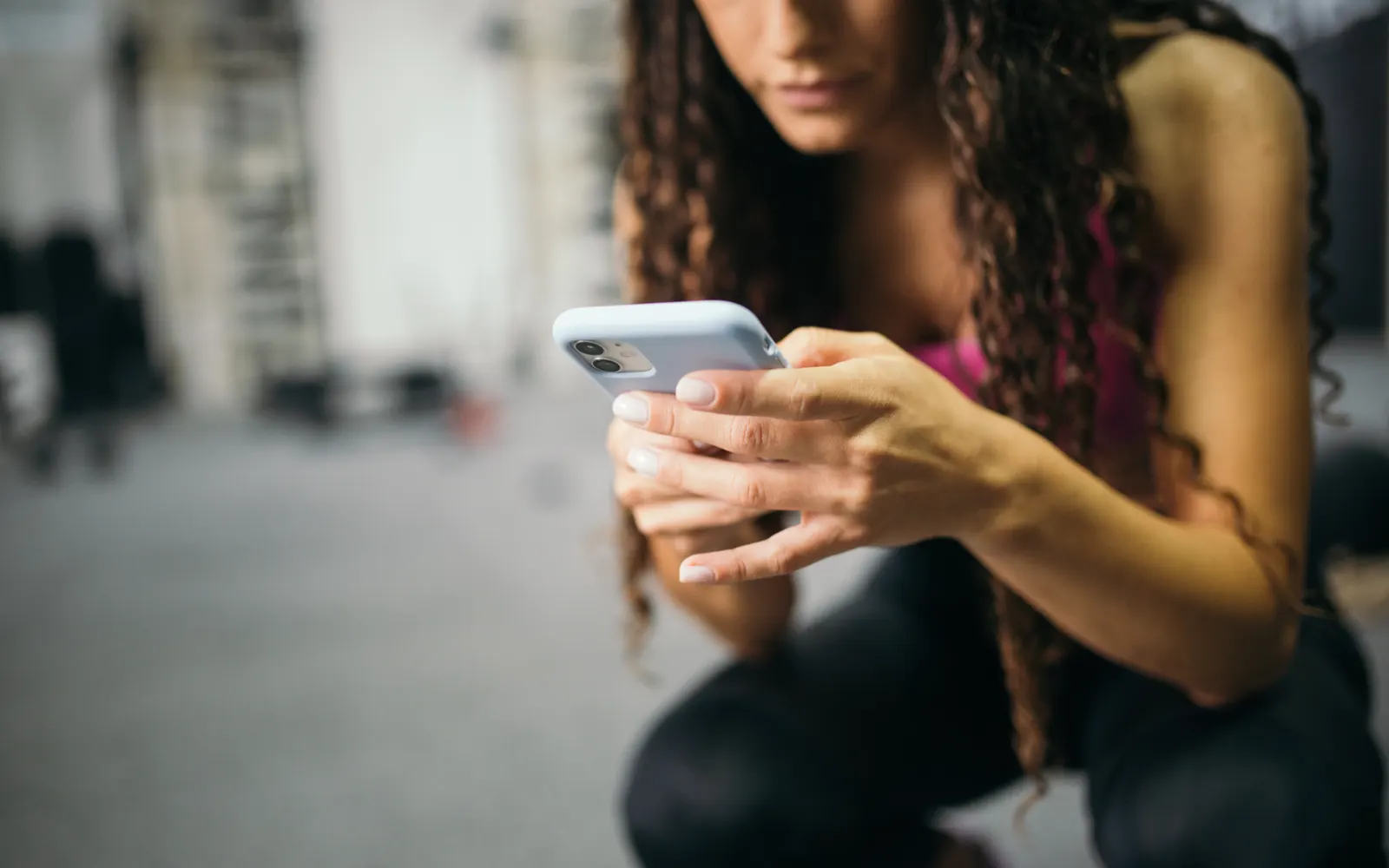 A woman with curly hair crouching down while checking her phone