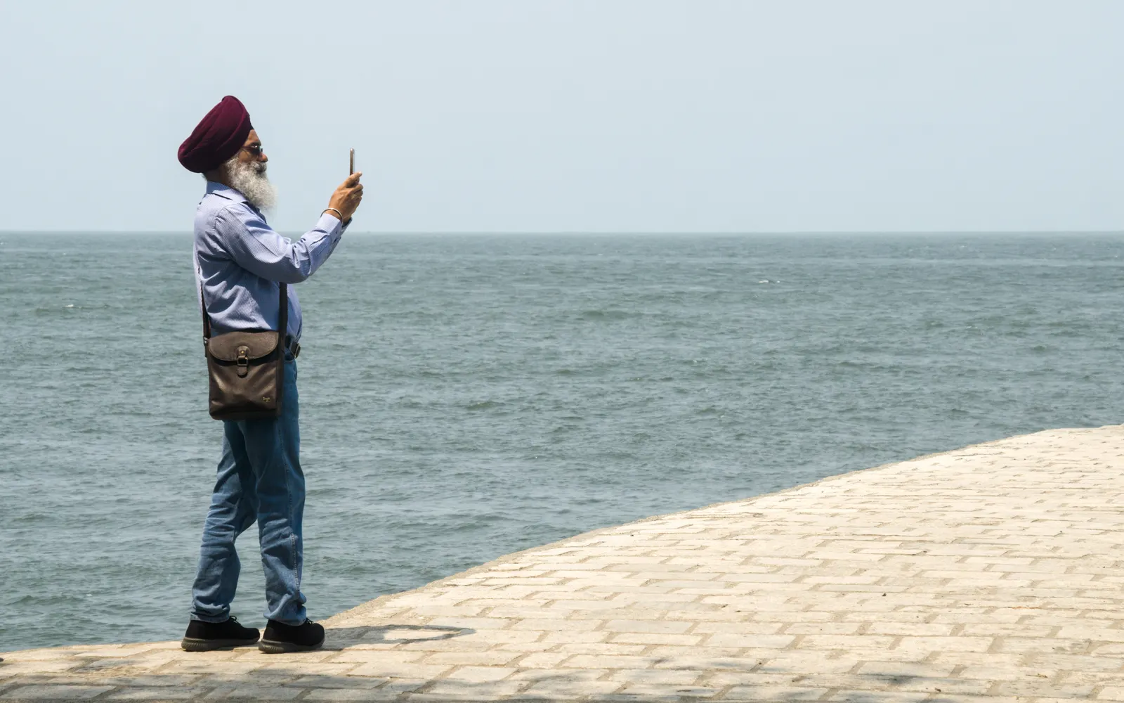 A man in a turban taking a photo of the sea with his phone