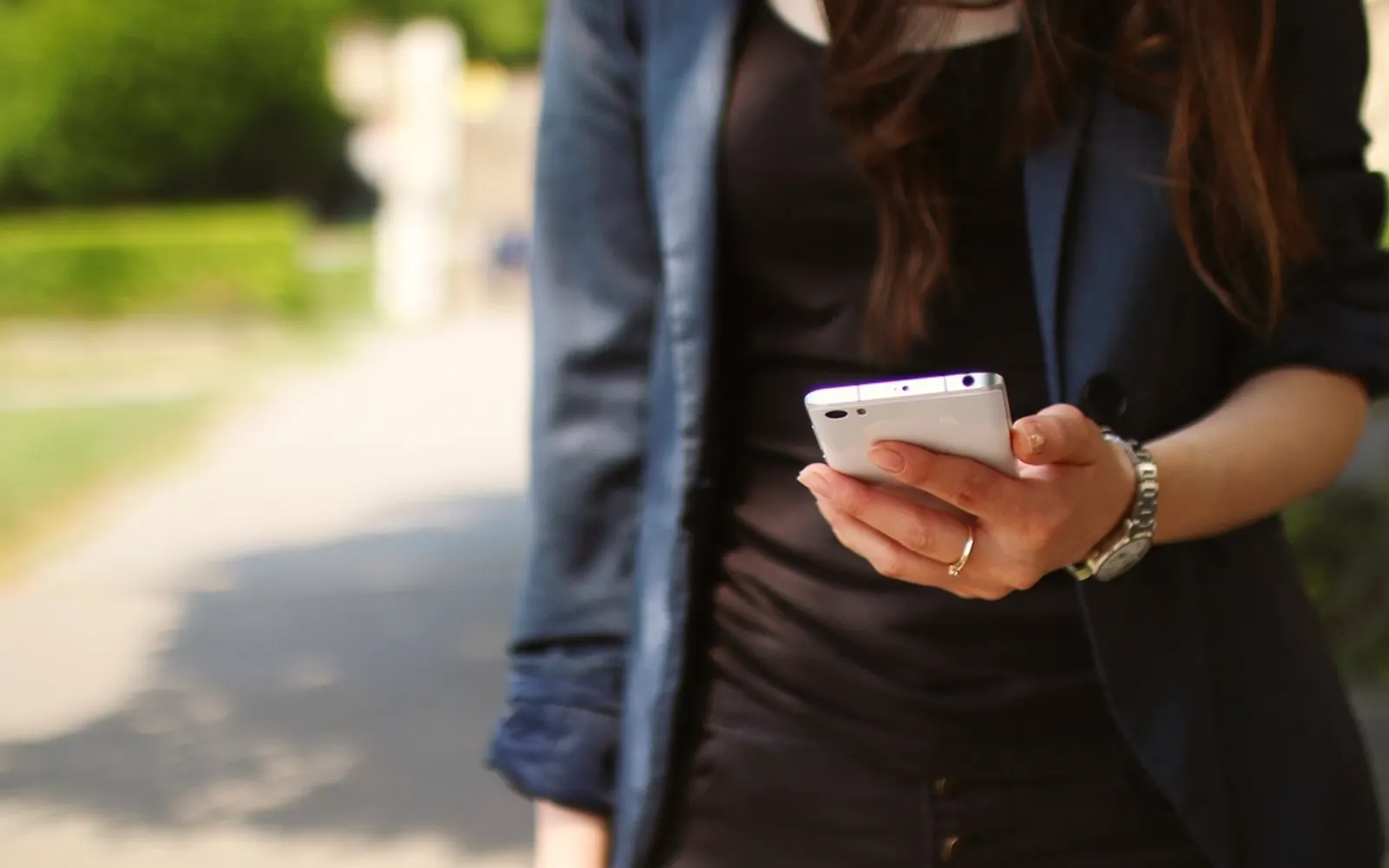 A woman in a blazer walking outdoors while checking her phone